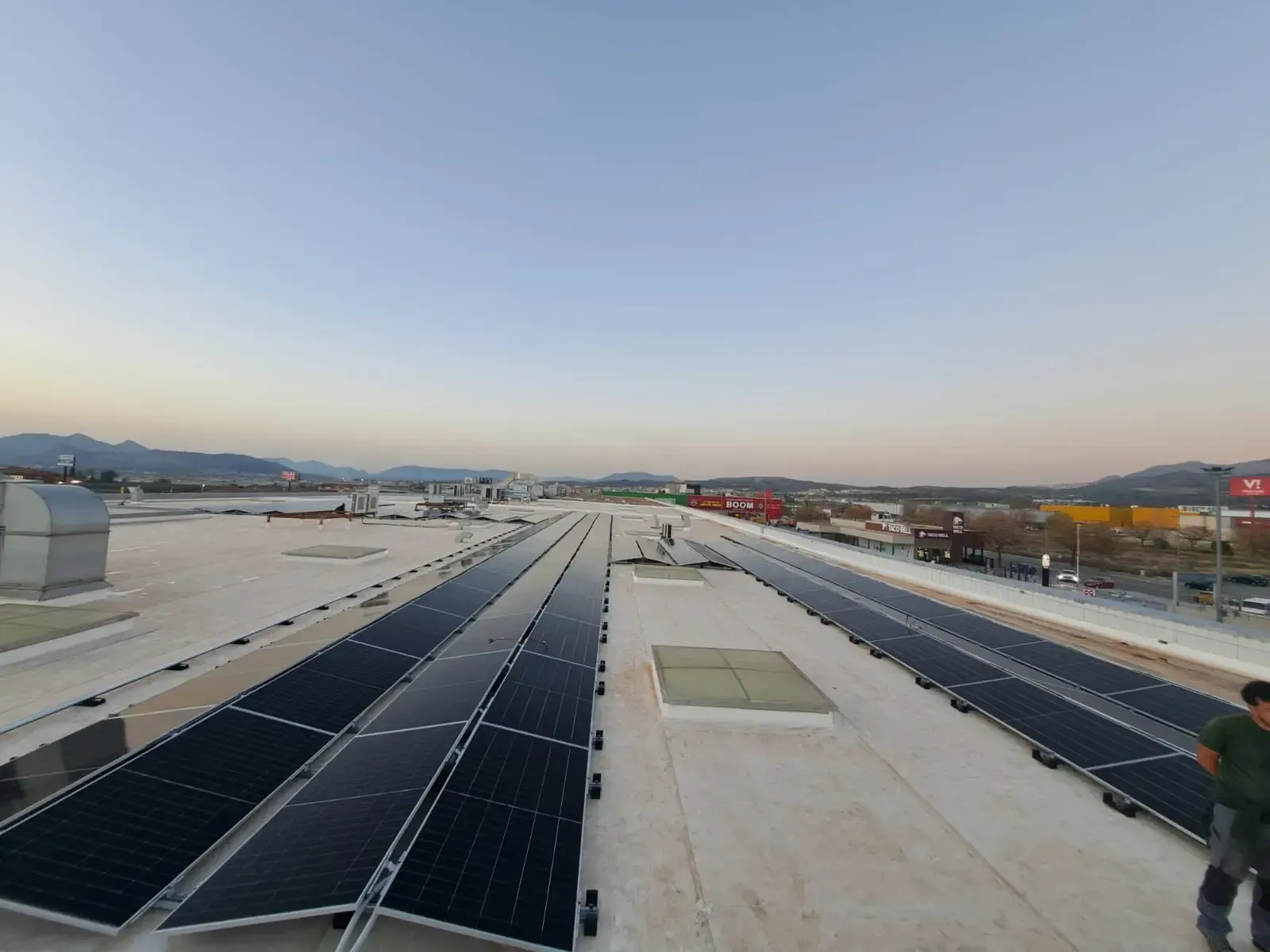 Azotea con hileras de paneles solares bajo un cielo despejado, con una persona en el extremo derecho.