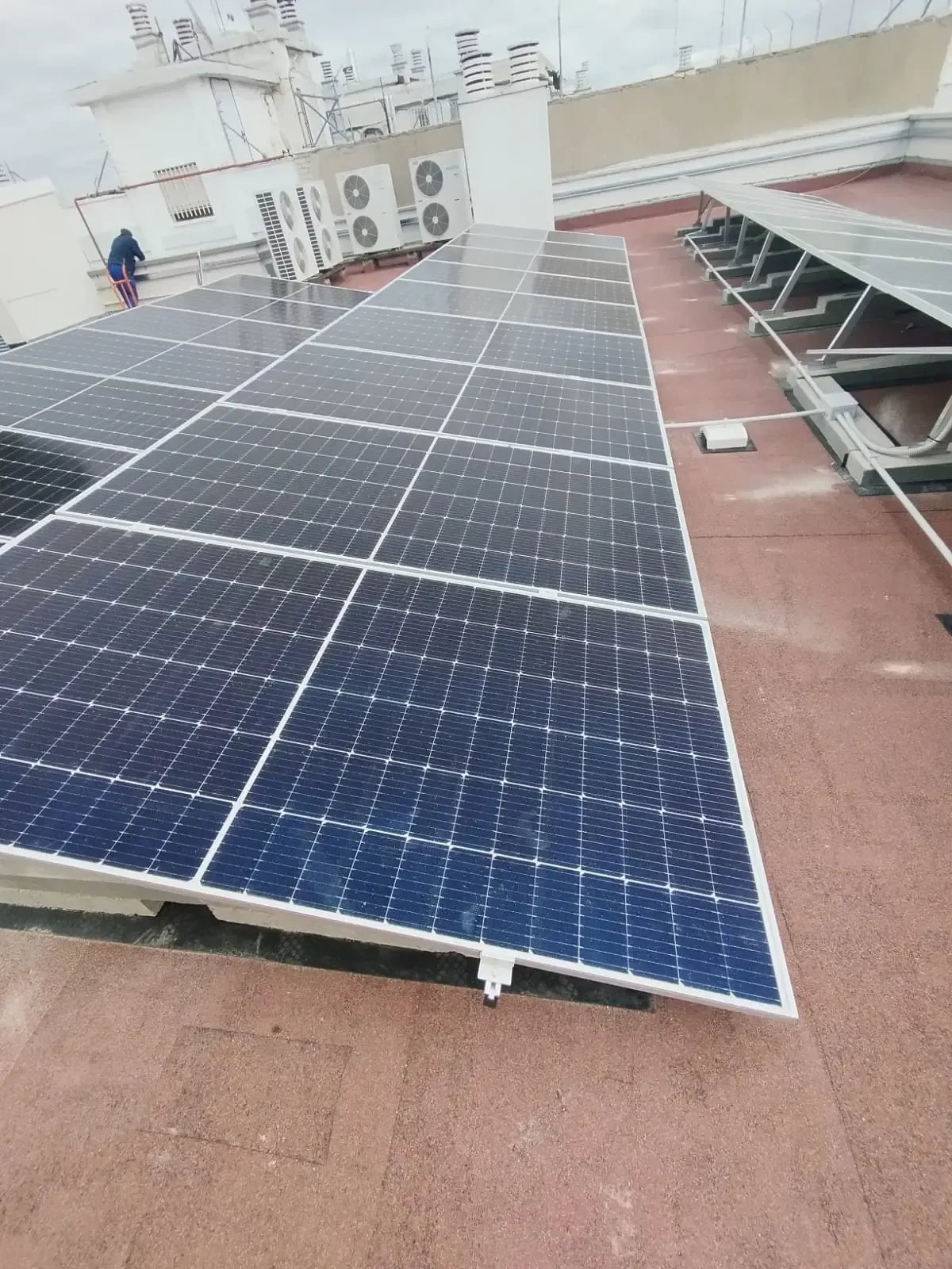 Paneles solares instalados en una azotea junto a una pasarela roja y edificios cercanos.