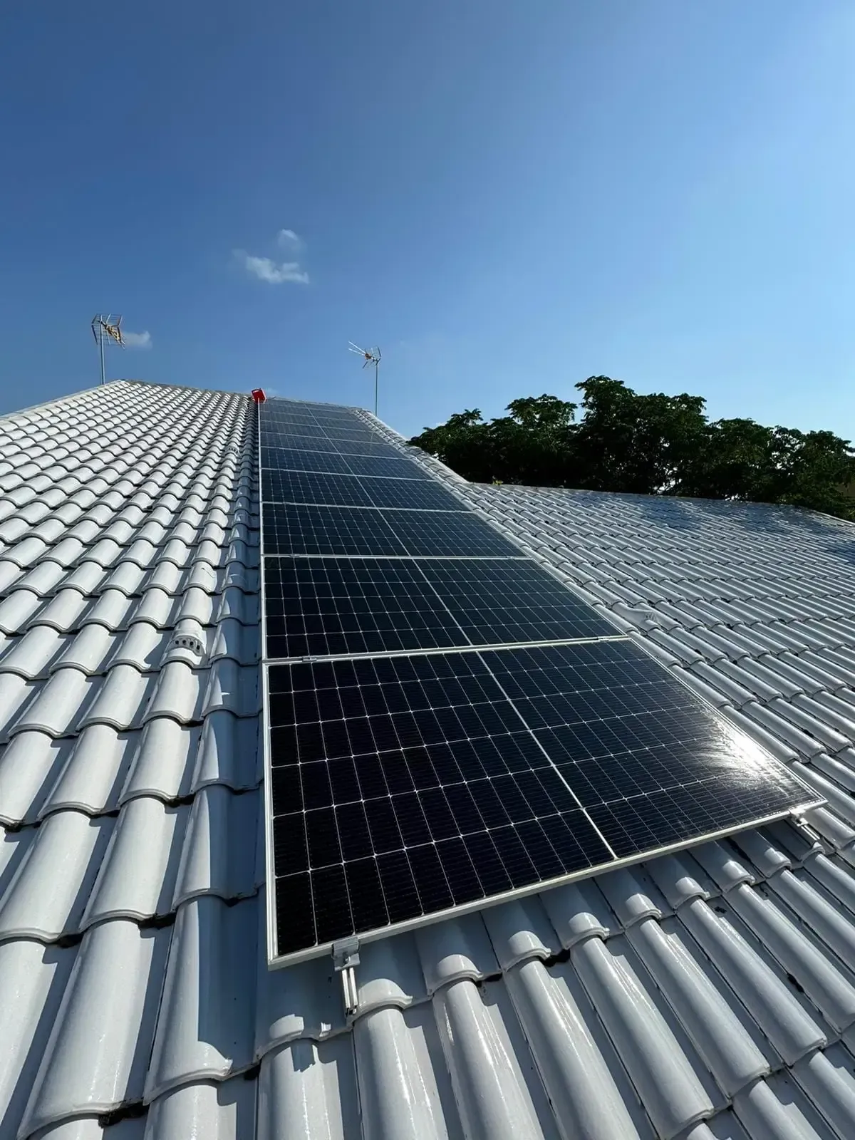 Paneles solares sobre un tejado de tejas blancas bajo un cielo azul despejado.