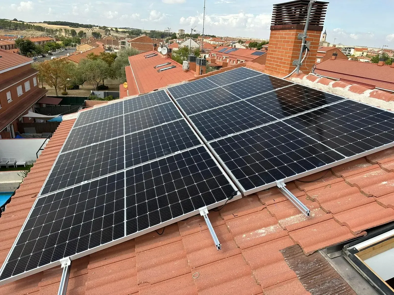 Paneles solares instalados en un tejado de tejas rojas bajo un cielo brillante.