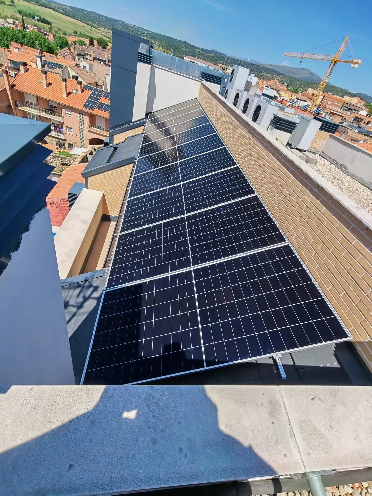 Paneles solares instalados en un tejado inclinado con vistas a un pueblo y a colinas lejanas.