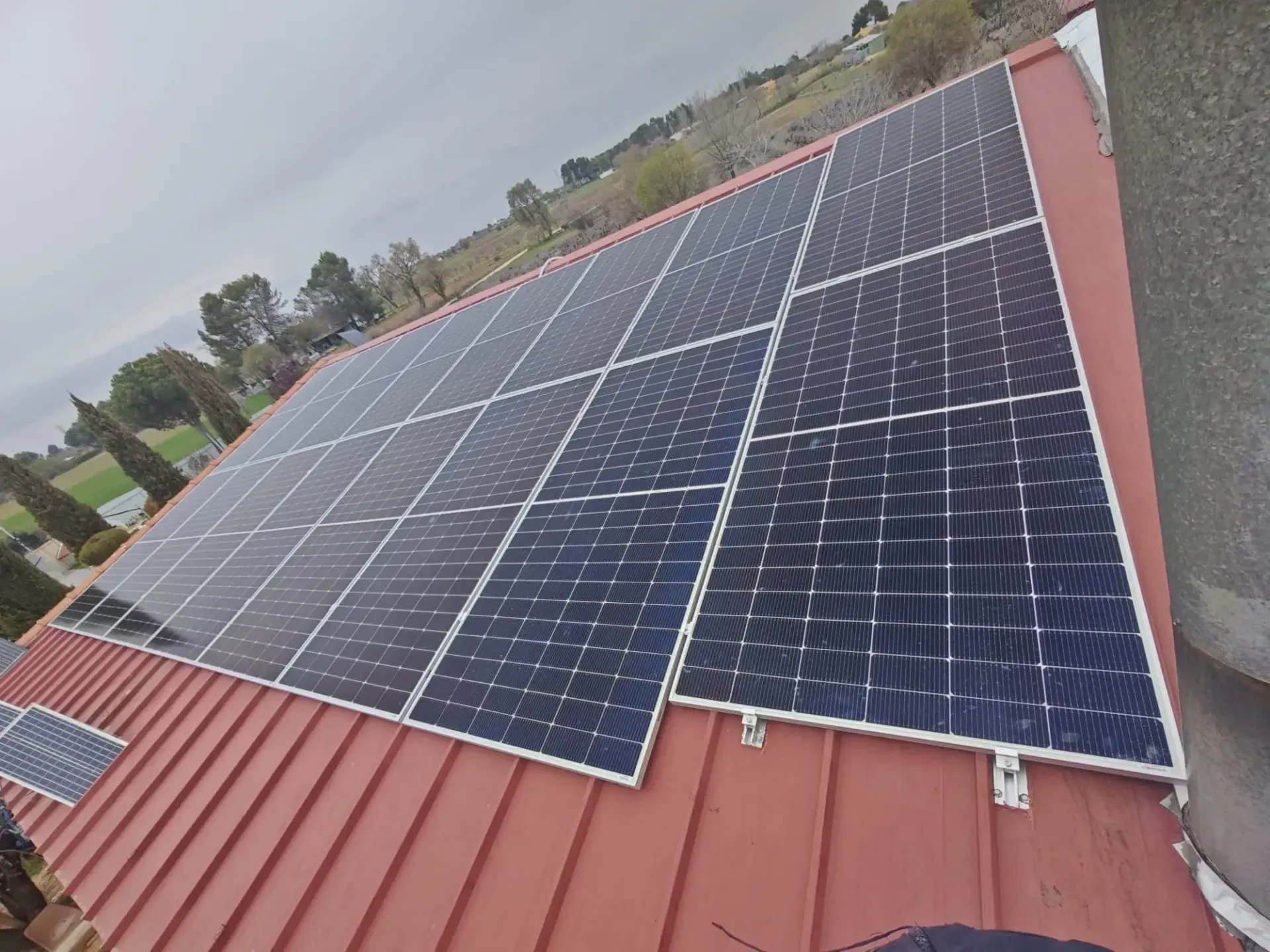 Paneles solares instalados en un techo de chapa ondulada roja bajo un cielo nublado.