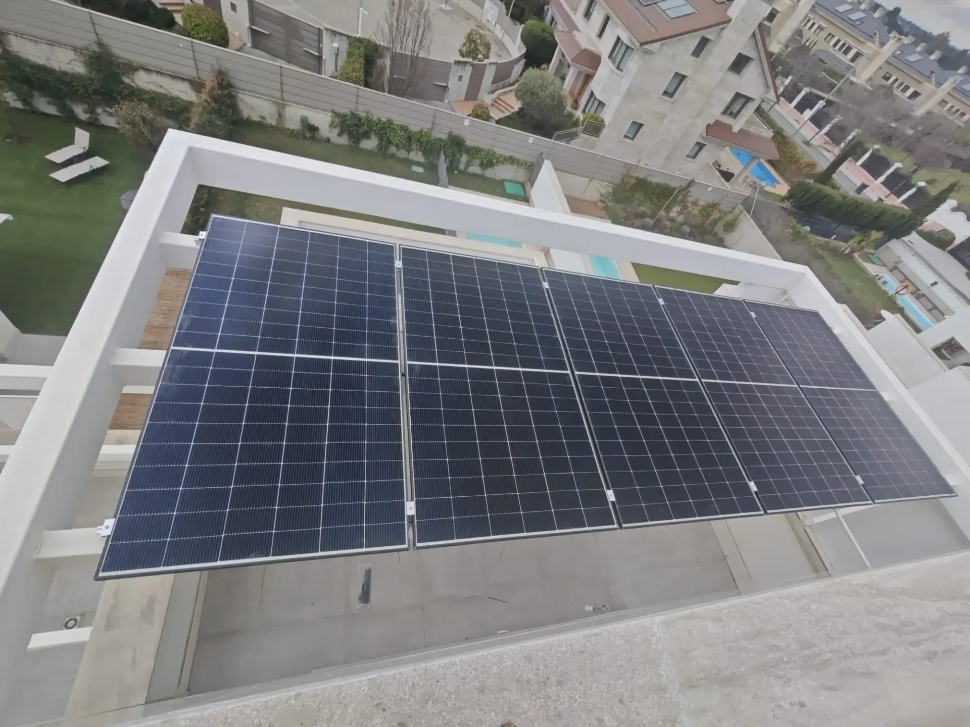 Paneles solares instalados en una azotea, vistos desde arriba con edificios y árboles al fondo.