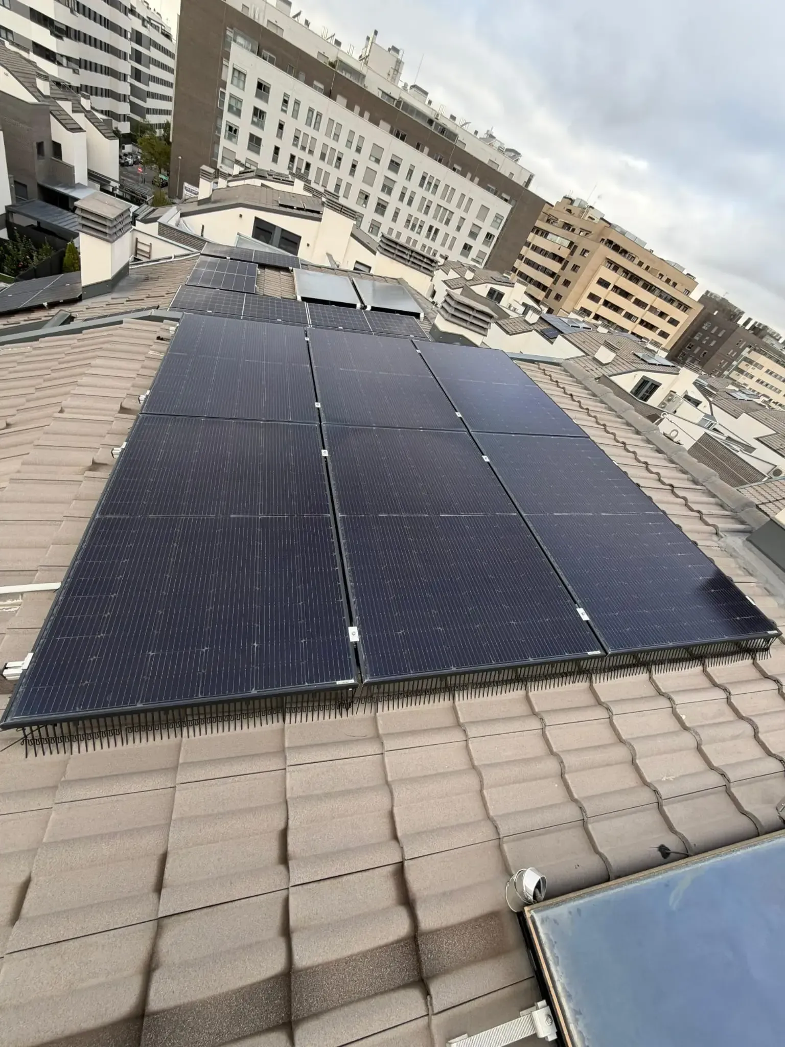 Paneles solares en una azotea con vistas a los edificios de apartamentos cercanos bajo un cielo nublado.