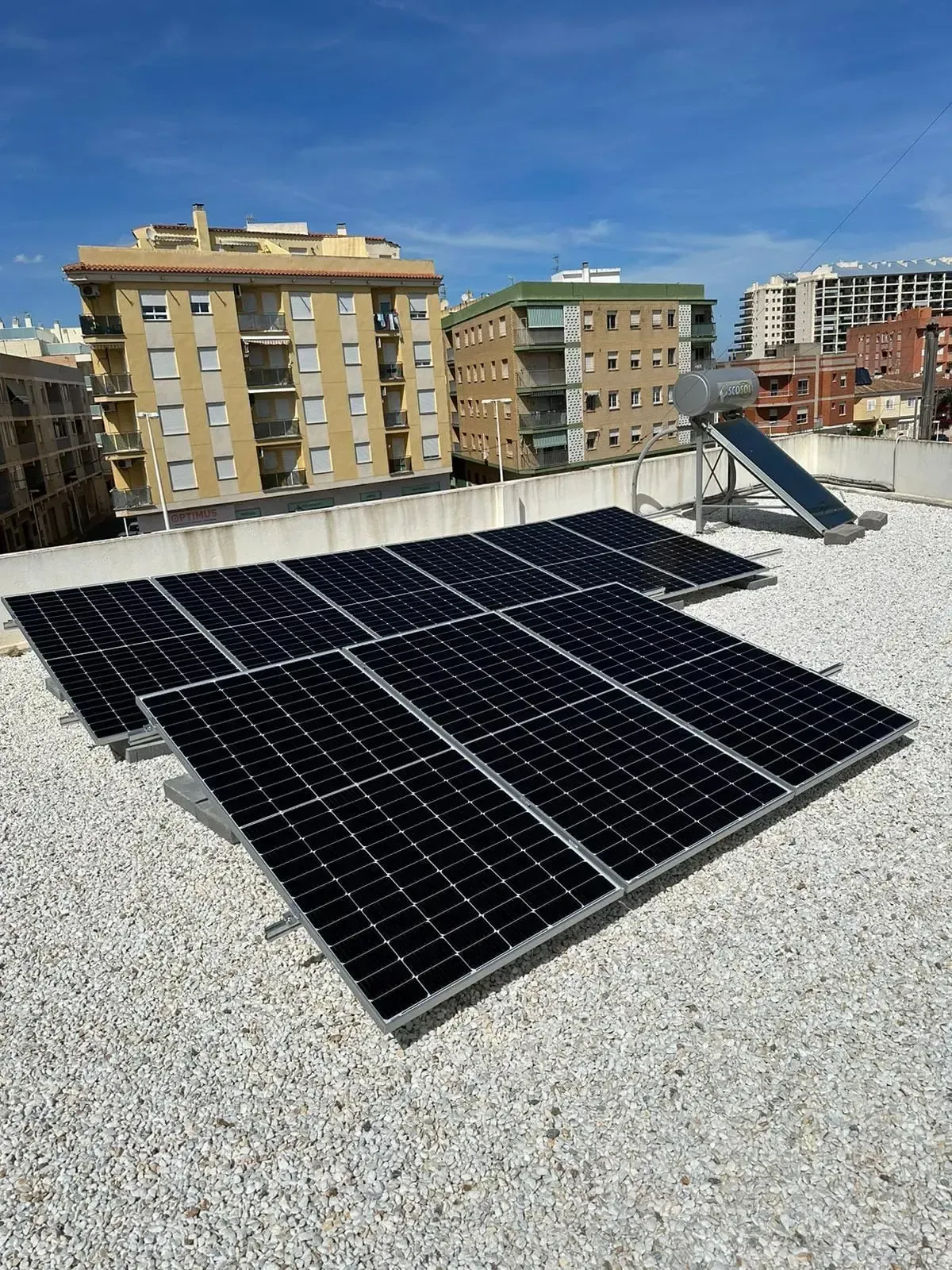 Paneles solares en un tejado de grava con edificios de apartamentos al fondo.