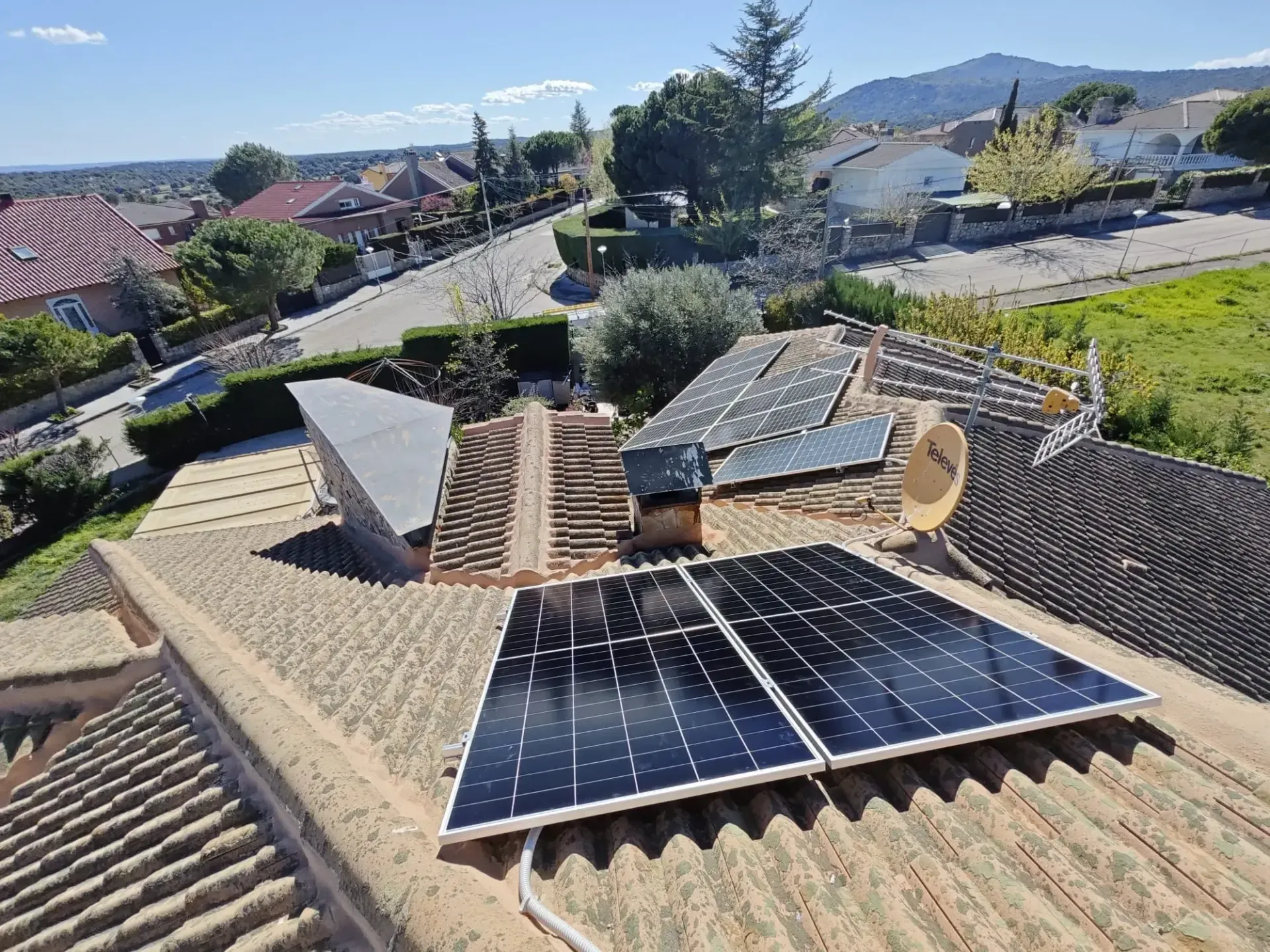 Paneles solares en el tejado de una casa con tejas en un barrio residencial, con montañas al fondo.