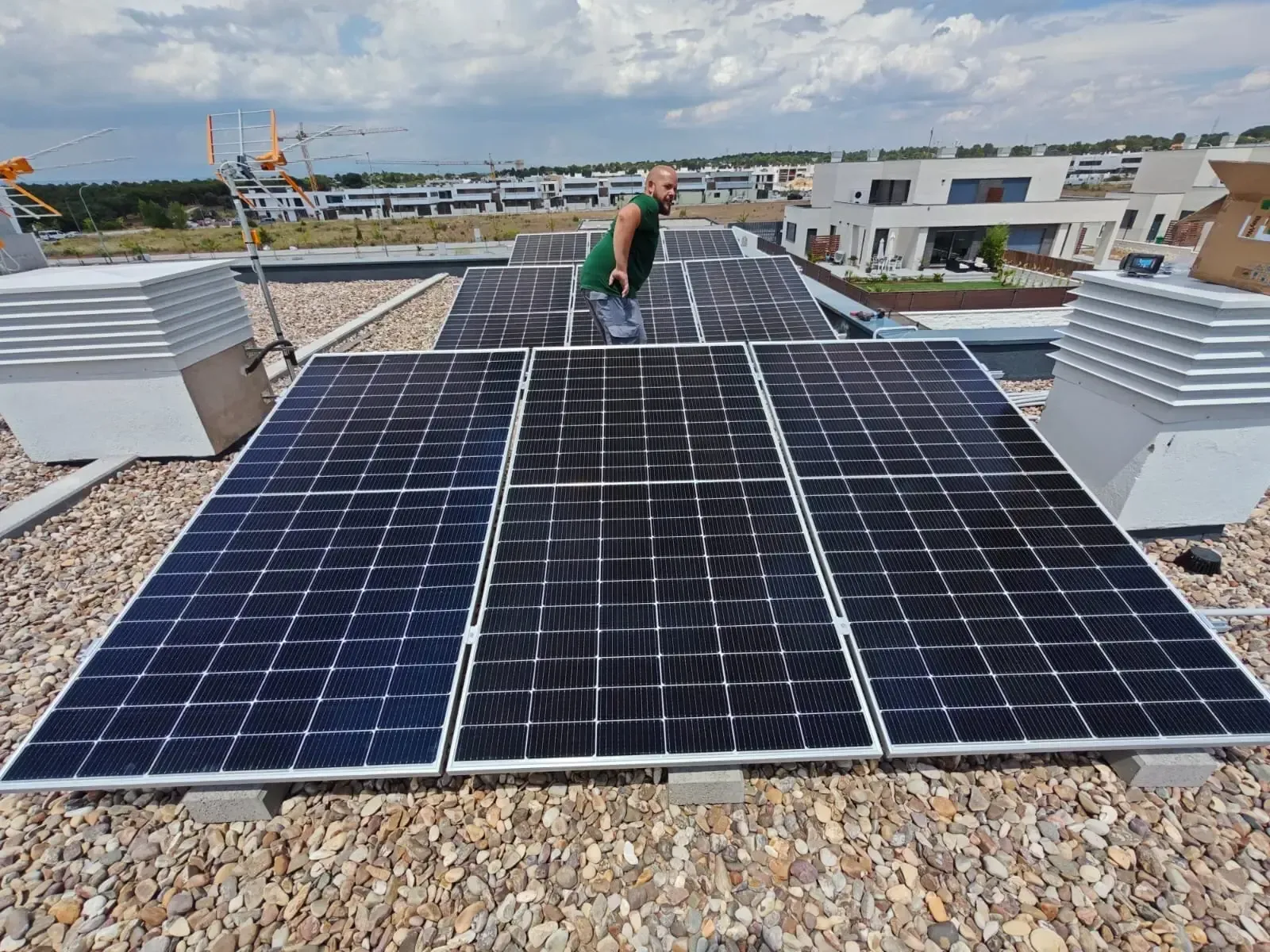 Paneles solares en una azotea, con un trabajador al fondo bajo un cielo nublado.