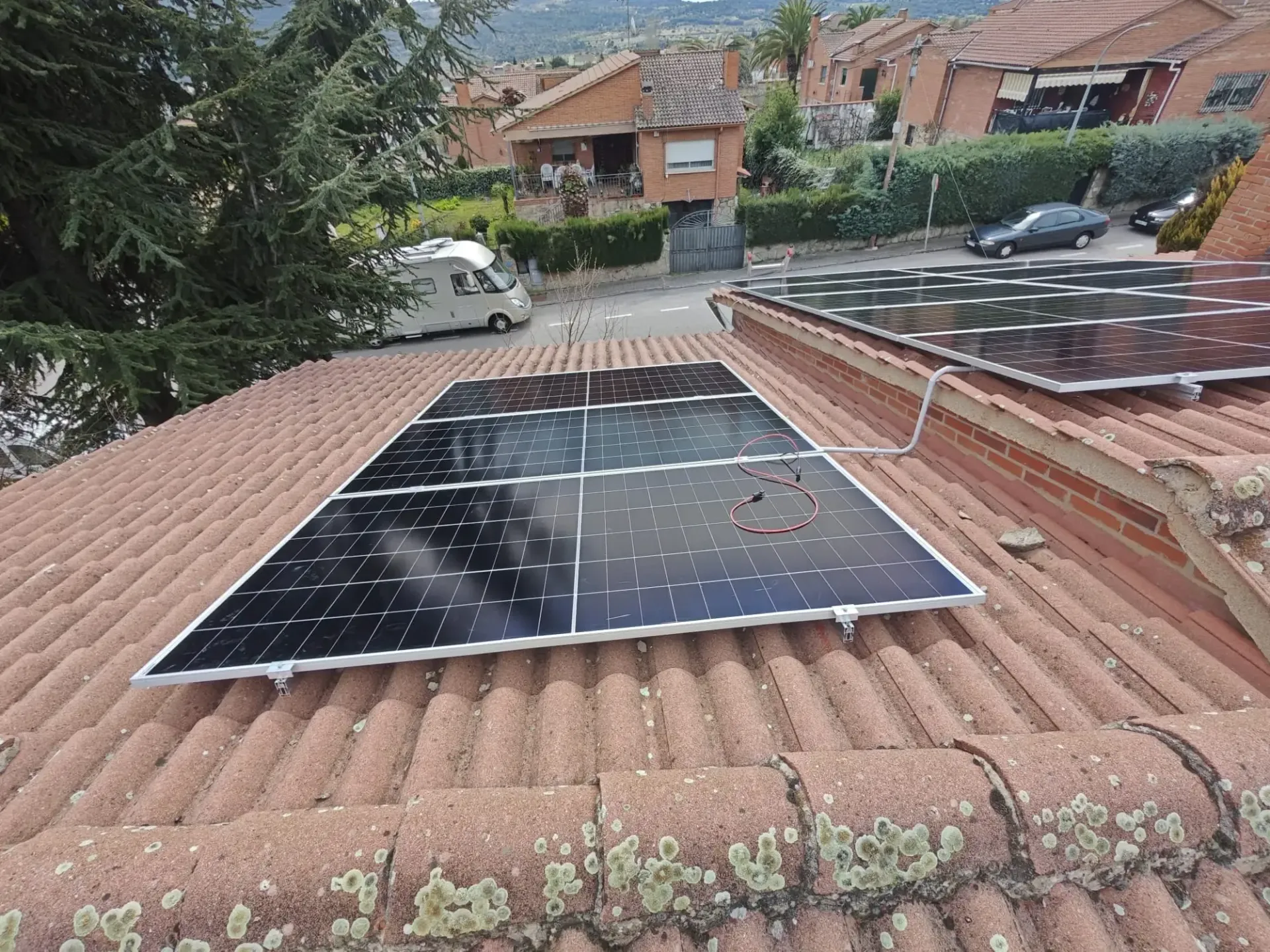 Paneles solares instalados en un tejado de tejas rojas con vistas a una calle residencial.