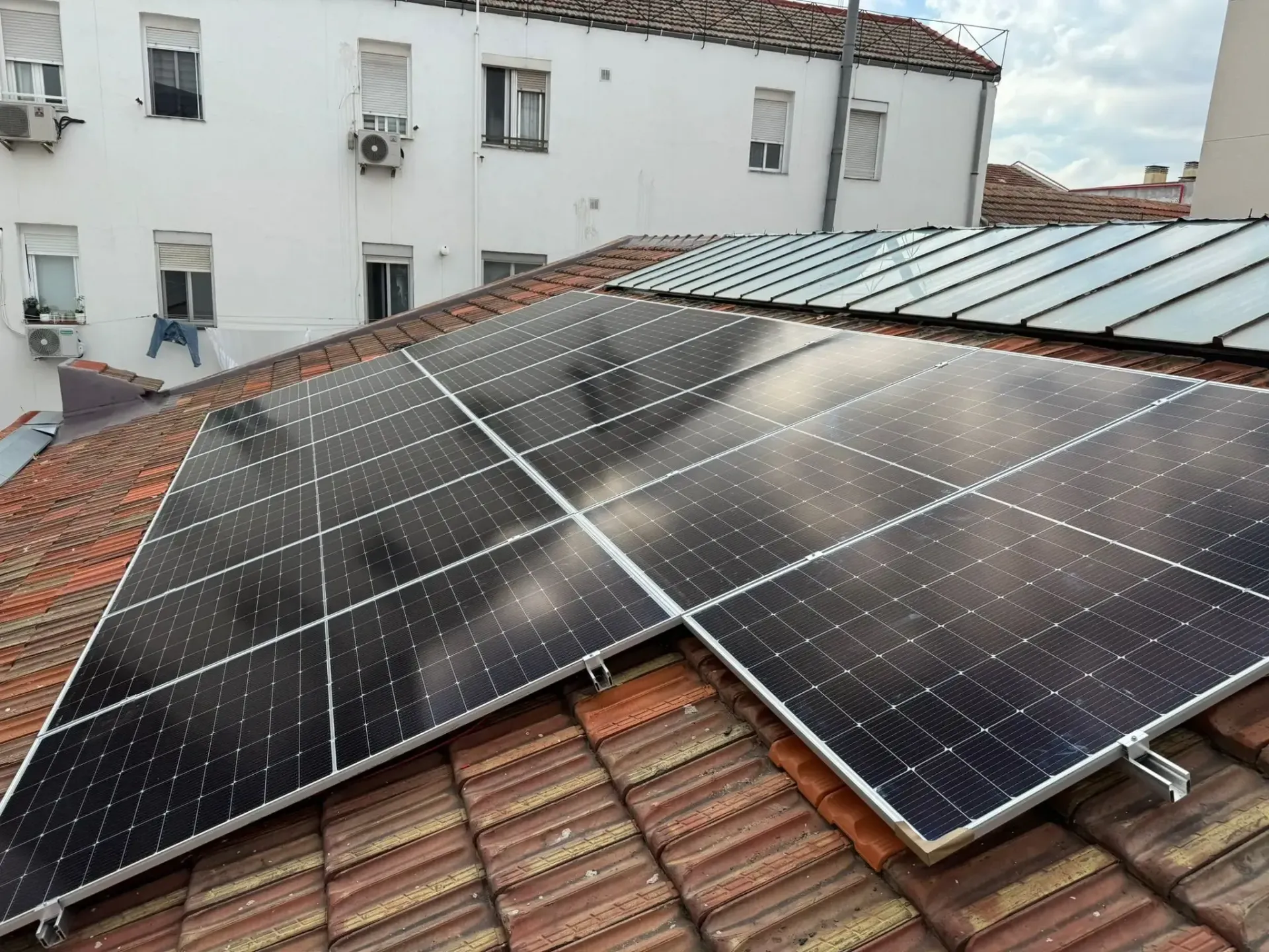 Paneles solares instalados en un tejado de tejas rojas junto a un edificio blanco.
