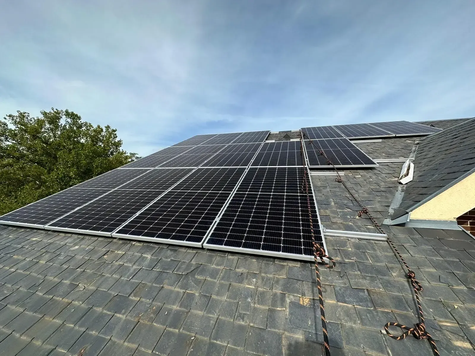 Paneles solares instalados en un tejado de tejas grises bajo un cielo parcialmente nublado.
