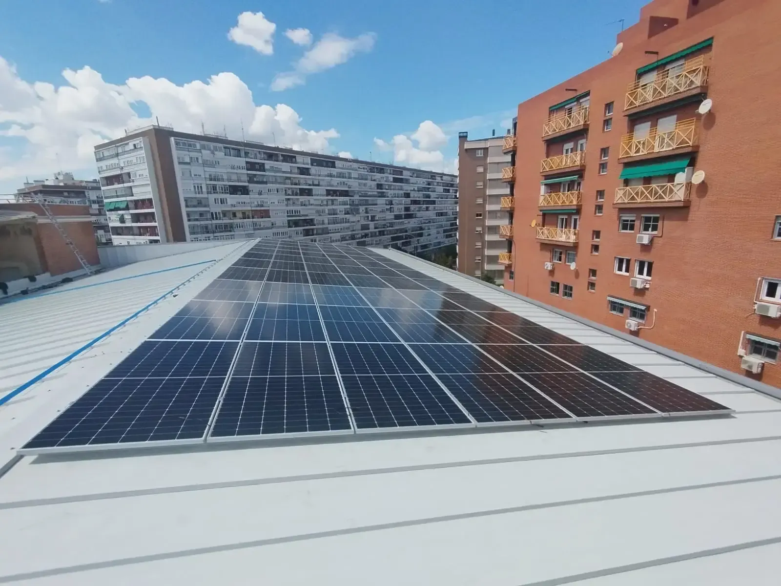 Paneles solares en una azotea con edificios de apartamentos en la ciudad bajo un cielo azul con nubes.