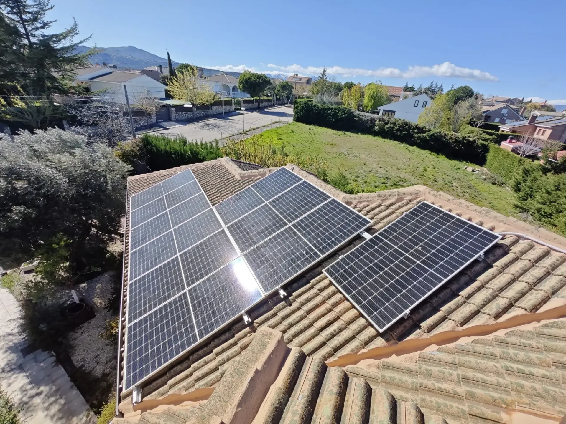 Paneles solares en un tejado de tejas con vistas a una soleada ladera suburbana.