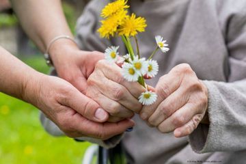 SaL-Dienstleistungs GmbH Seniorin hält selbstgepflückte Blumen, eine Pflegerin hält ihre Hand