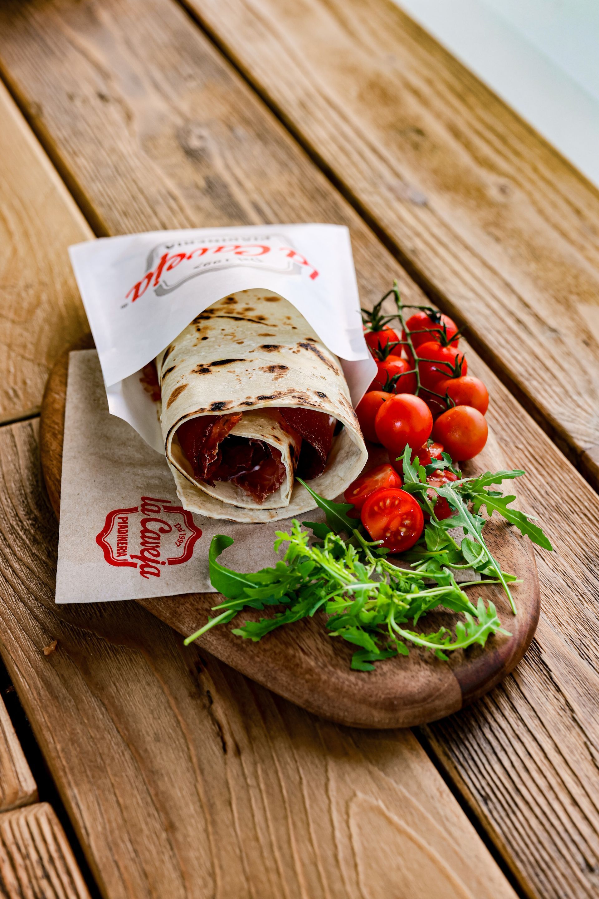 Una Piadina - La Caveja Lugano -  con carne e pomodori su un tagliere di legno.