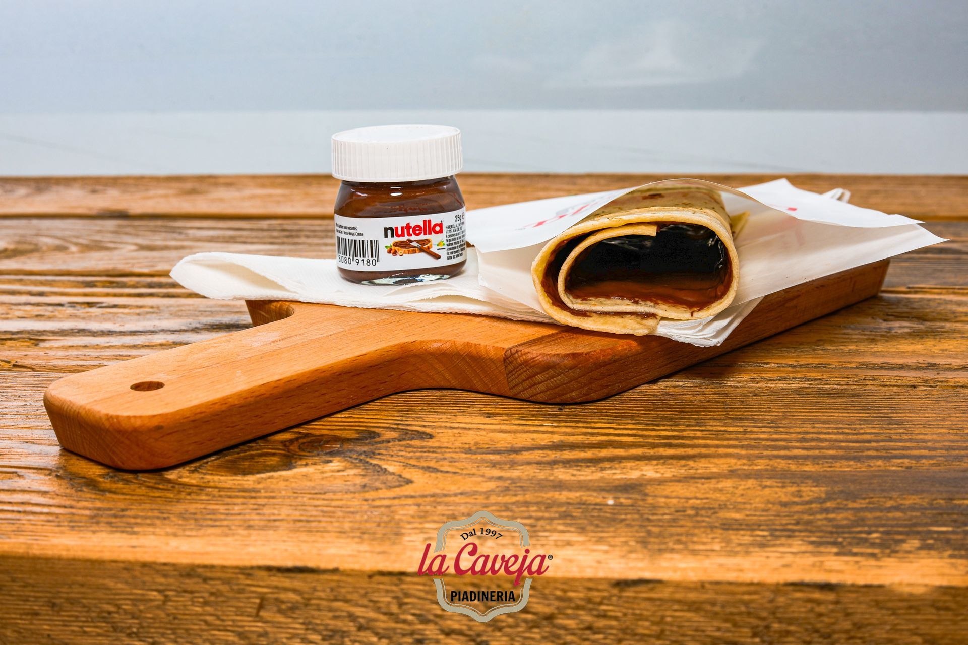 Una Piadina Romagnola e Nutella sono su un tagliere di legno.