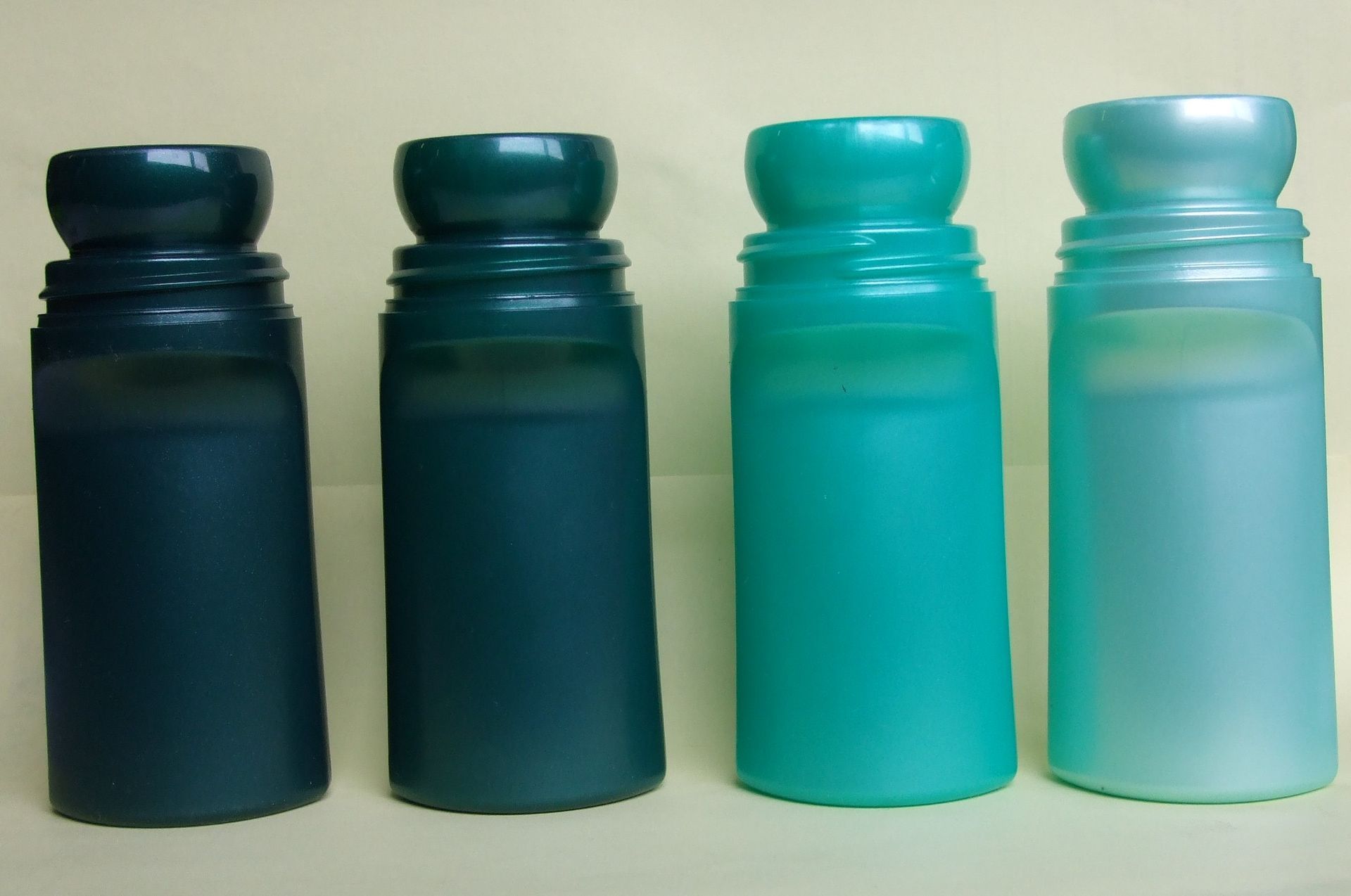 Quatre bouteilles d'eau translucides, dans des tons allant du bleu sarcelle foncé au bleu clair, alignées sur une surface claire.