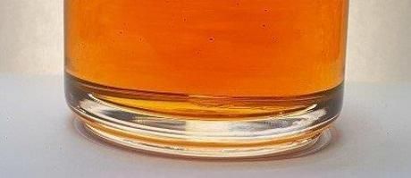 Gros plan d'un verre rempli d'un liquide ambré sur une surface blanche