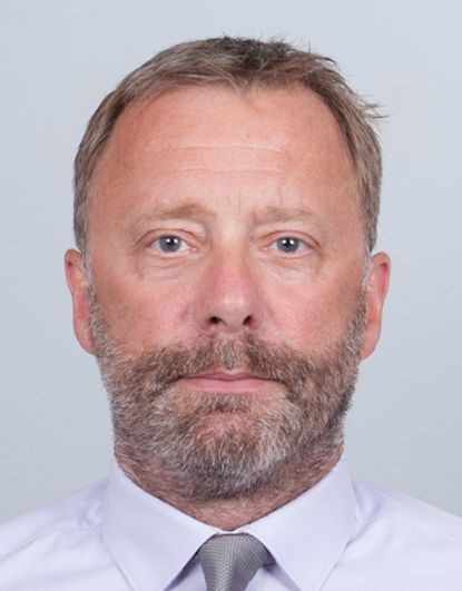 Portrait en buste d'un homme en chemise blanche et cravate sur fond gris clair.