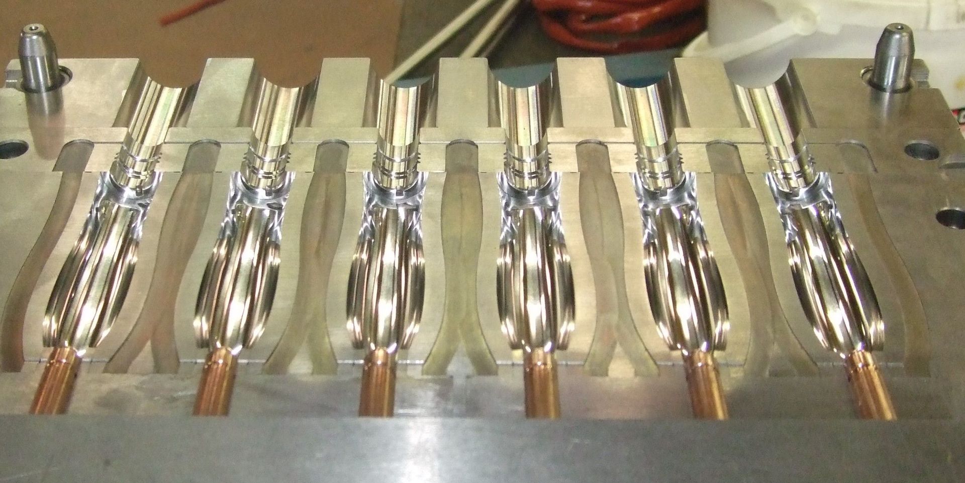 Des rangées de pinces métalliques brillantes à poignées en cuivre, fixées par des boulons sur un établi.