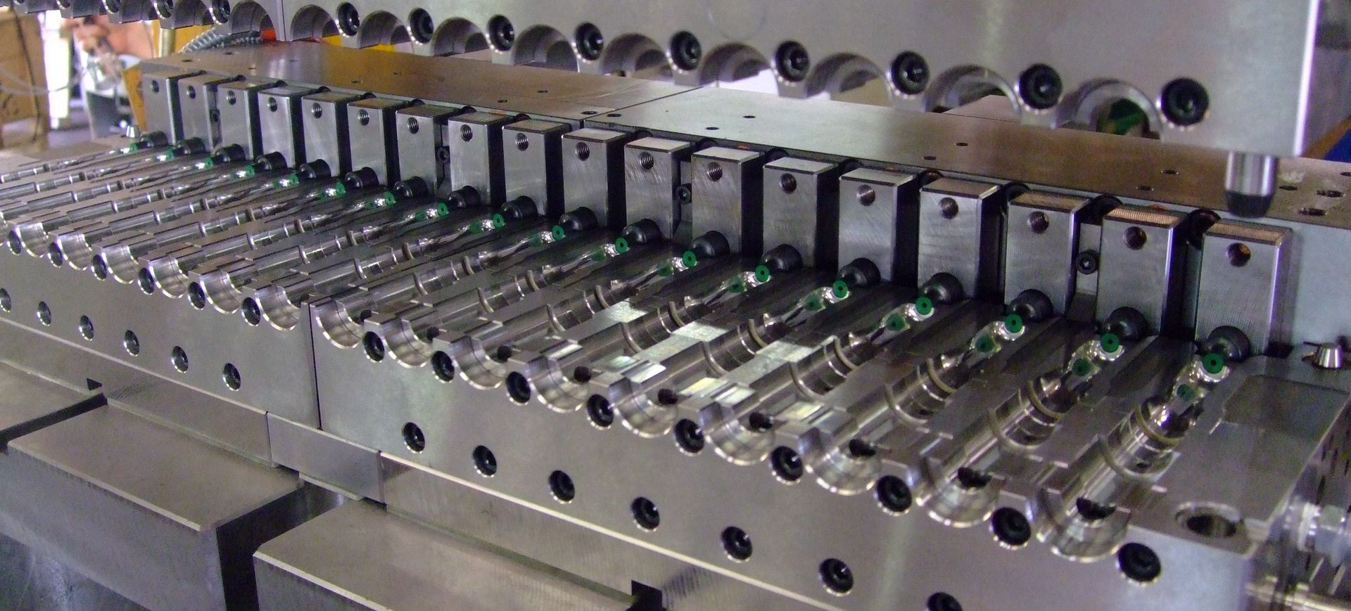 Machine industrielle avec des rangées de rouleaux métalliques et des composants verts dans un environnement d'usine