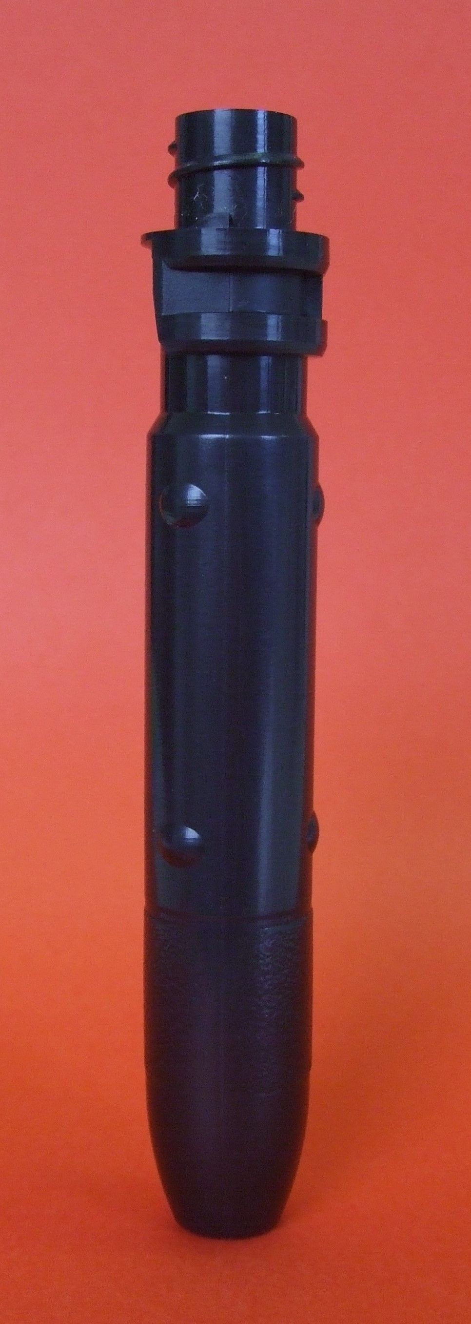 Outil ou cartouche cylindrique en plastique noir, debout sur un fond rouge