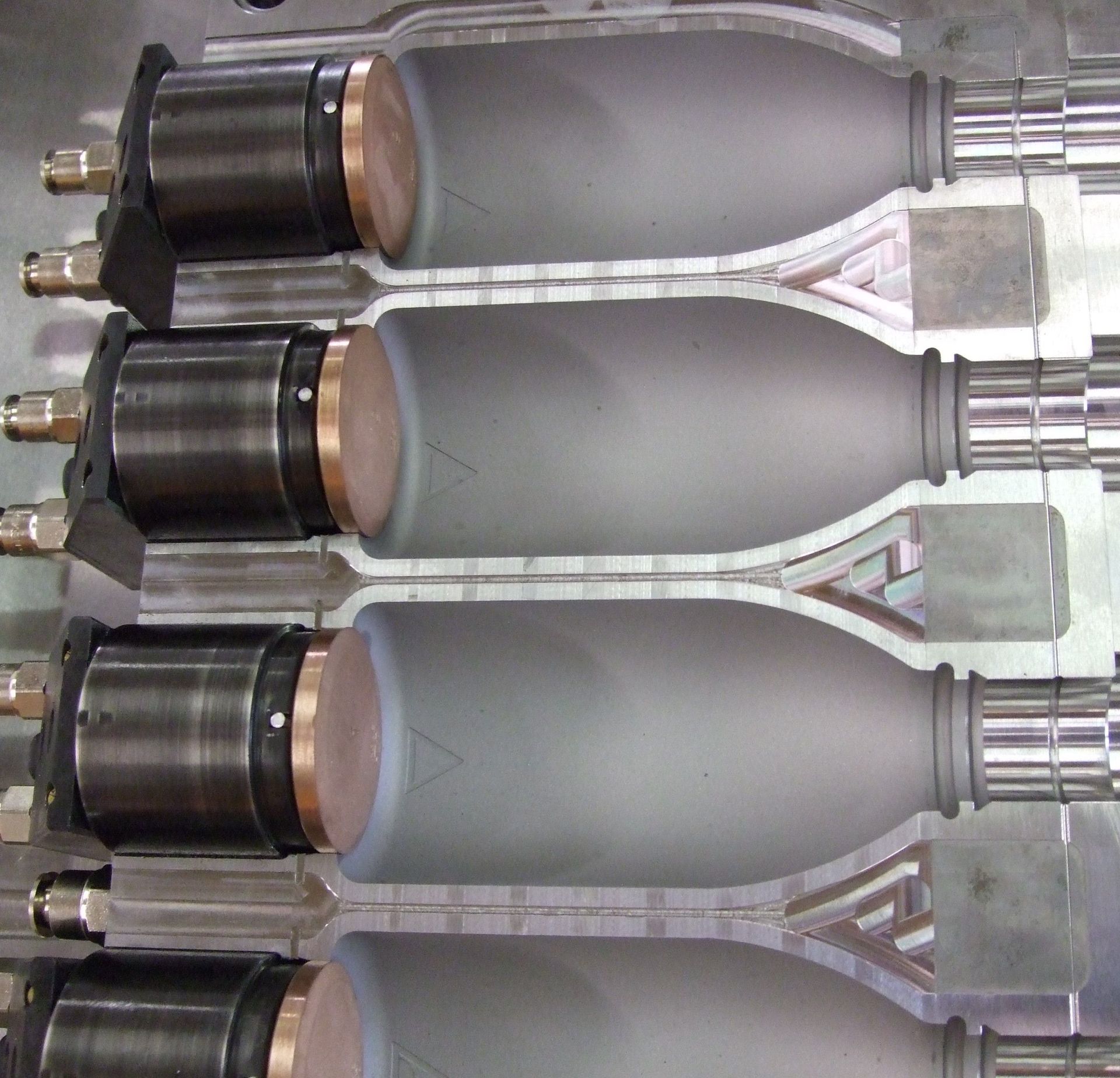 Des rangées de bombes aérosol grises sur une chaîne de production, avec des buses noires et des bouchons argentés.