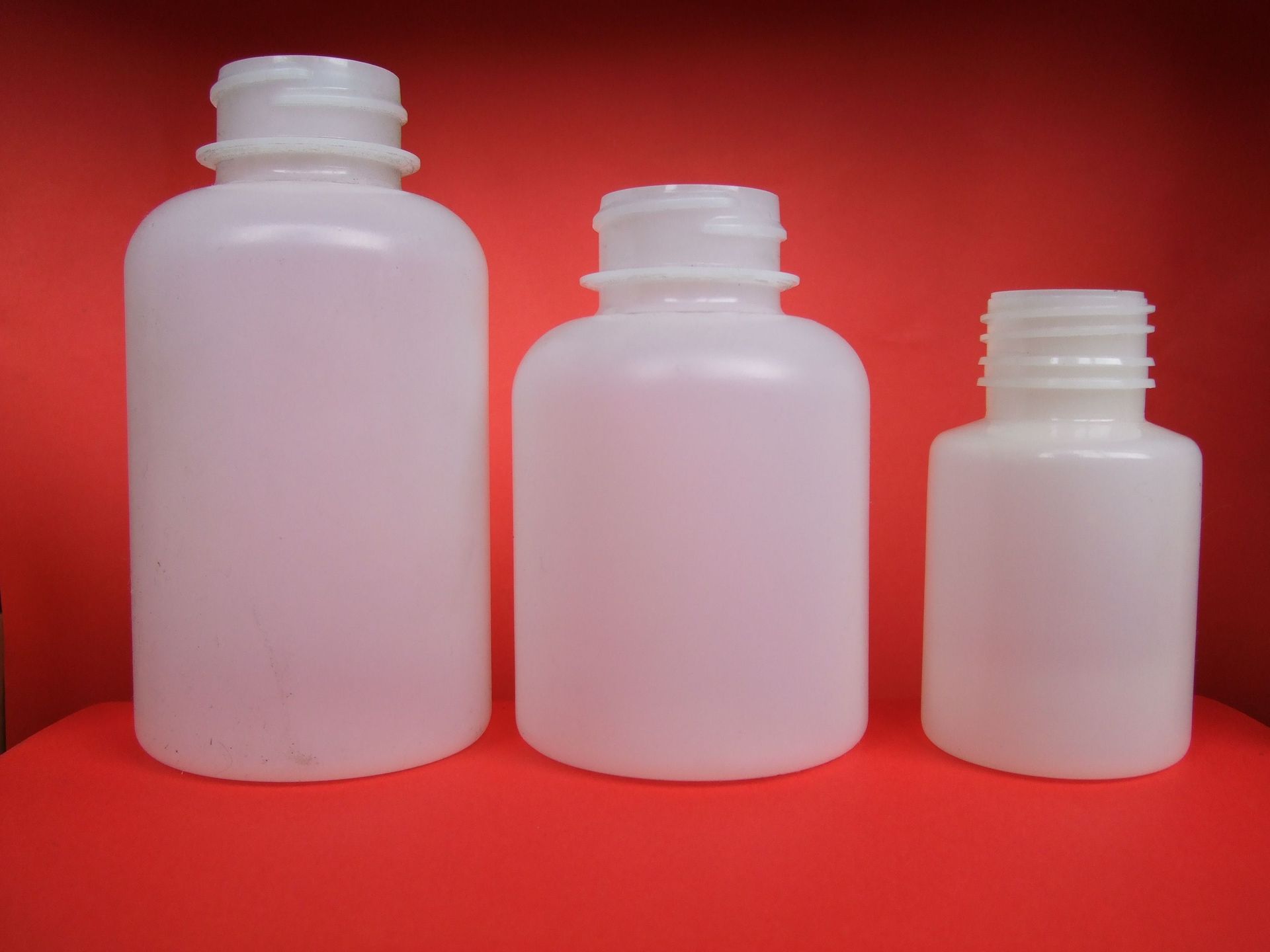 Trois bouteilles en plastique blanc de tailles différentes sur fond rouge.