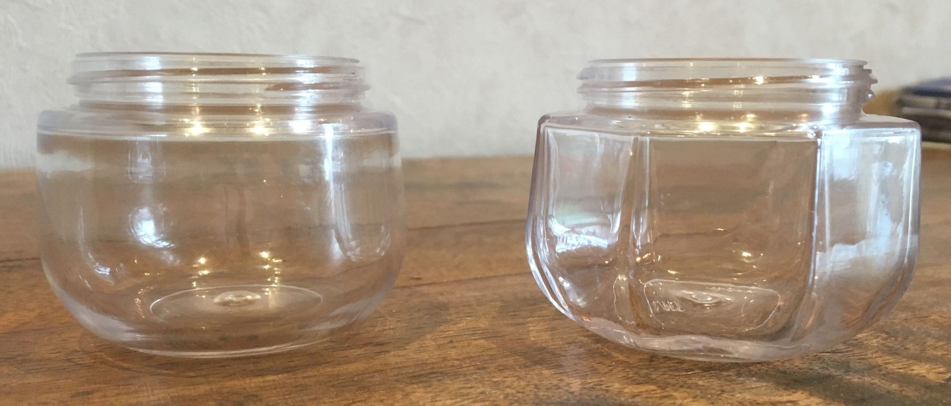 Deux bocaux en verre transparent posés sur une surface en bois, l'un arrondi et l'autre carré.