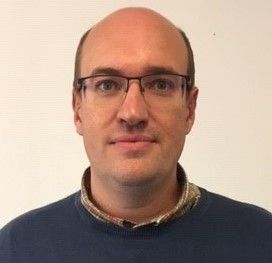 Portrait d'un homme portant des lunettes et un pull bleu marine sur fond blanc uni