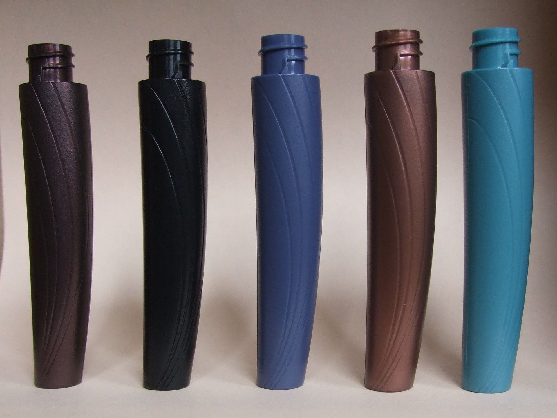 Cinq étuis ou bouteilles cylindriques aux motifs colorés, alignés sur un fond clair.