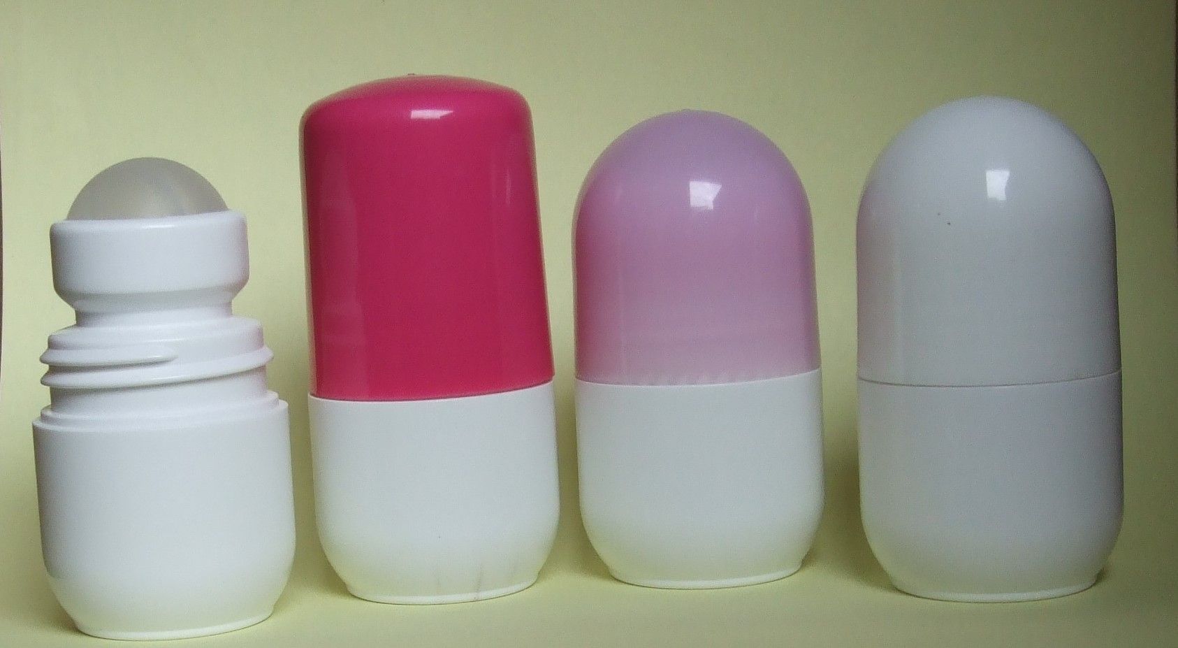 Quatre petits récipients en forme de pilule, à base blanche, un gris et trois à bouchon rose ou blanc, alignés sur une surface verte