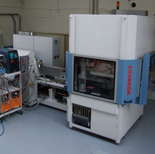 Machine industrielle dans un laboratoire, avec un boîtier blanc, un panneau latéral bleu et un équipement de contrôle à proximité.