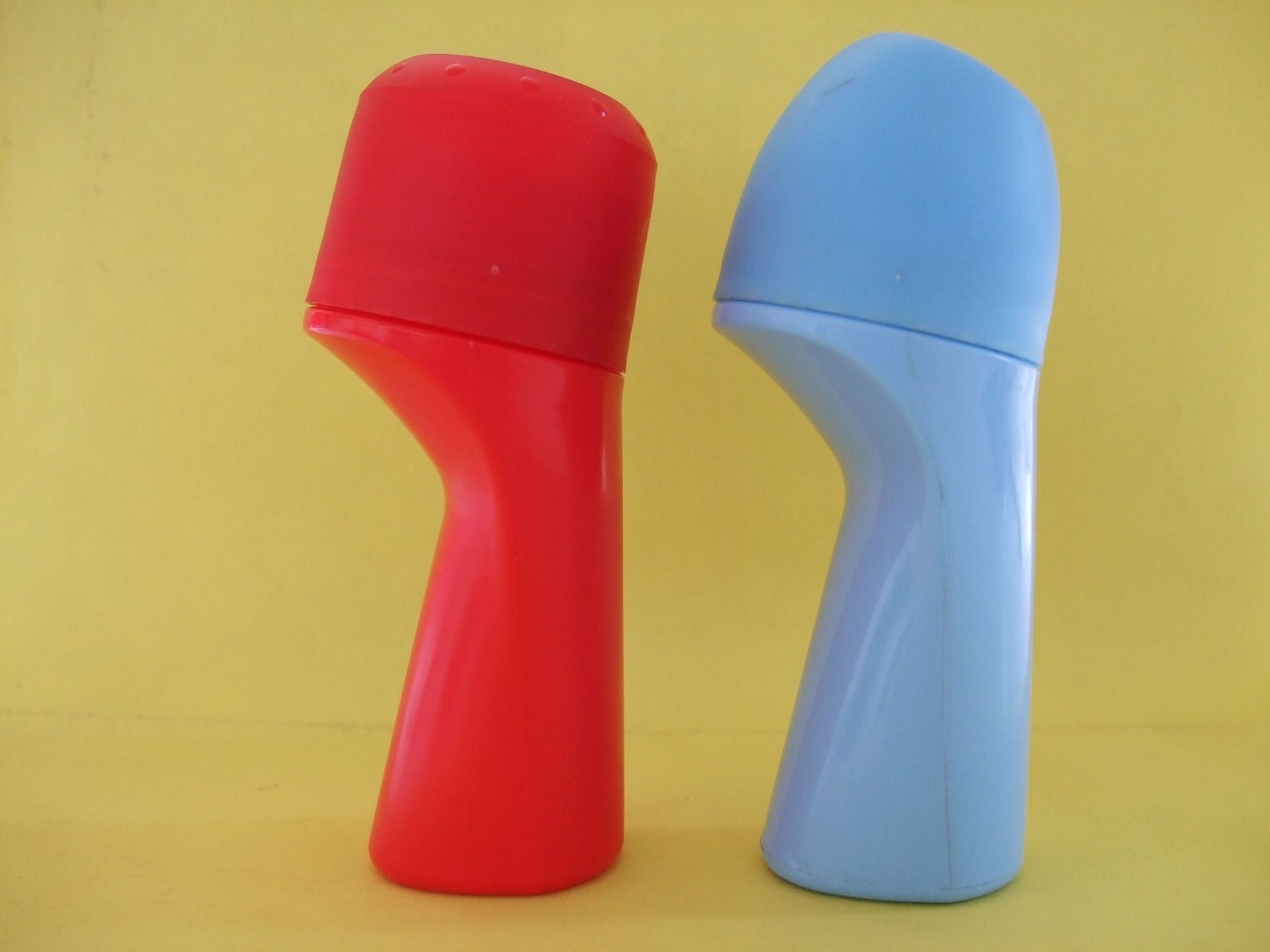 Deux objets colorés tenus à la main, l'un rouge et l'autre bleu clair, se tenant debout sur un fond jaune.