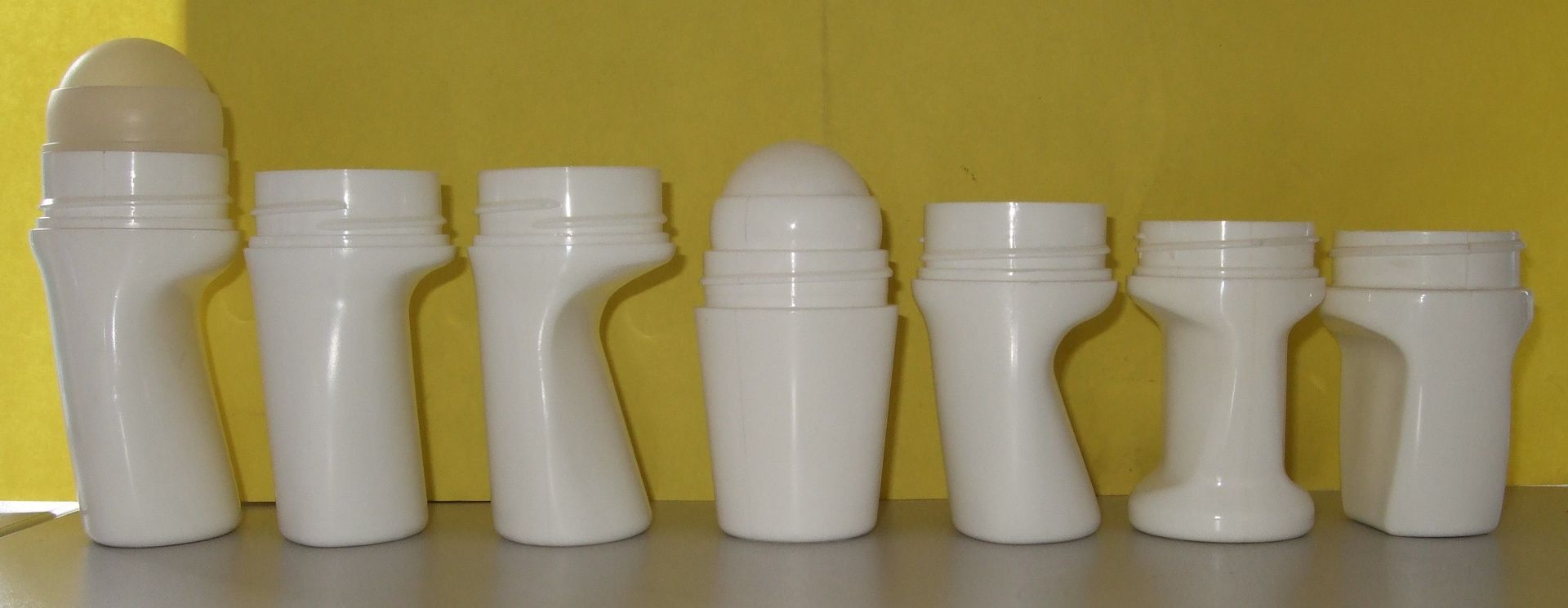 Sept flacons à condiments en plastique blanc alignés sur un fond jaune.