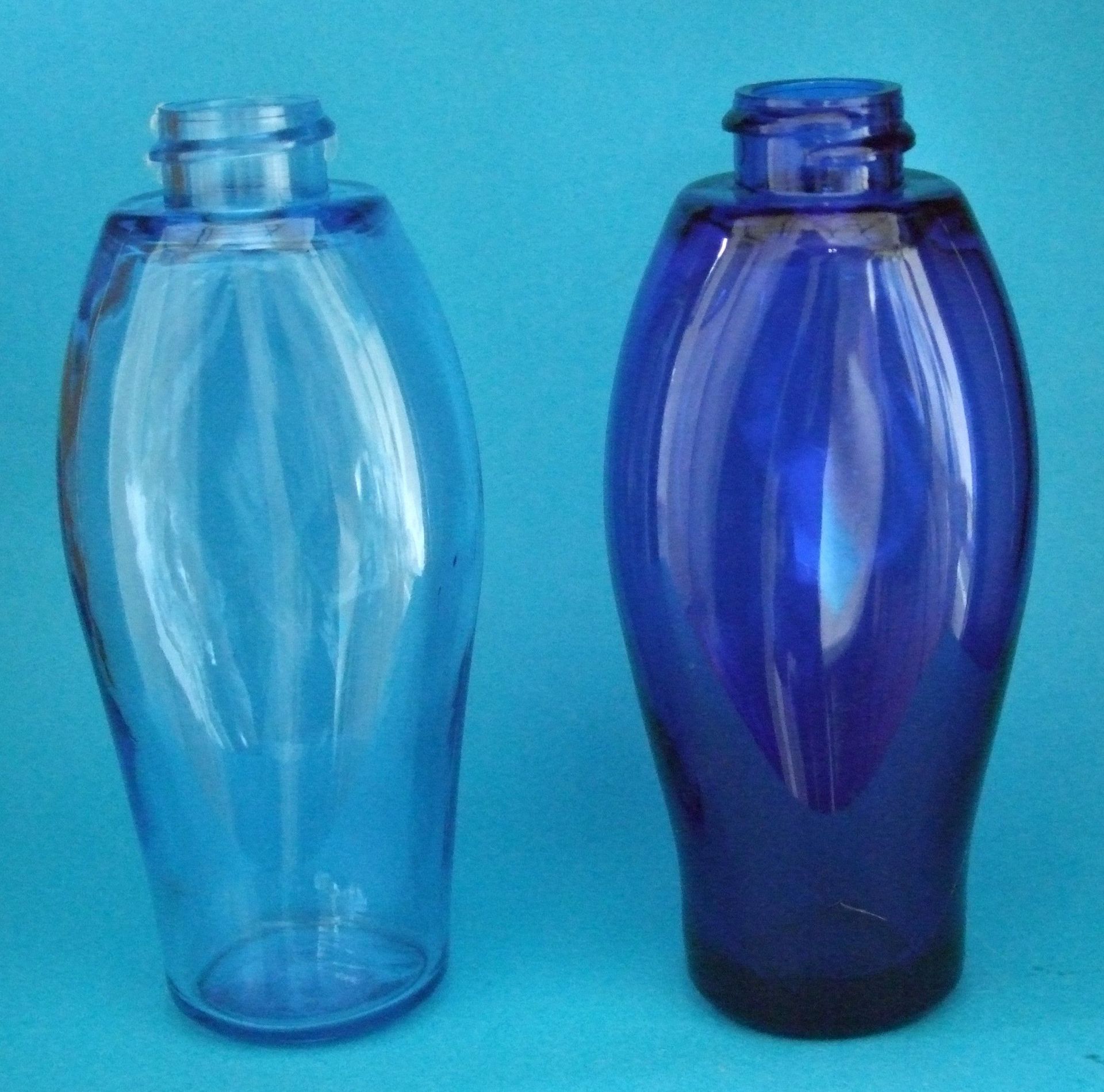 Deux bouteilles en verre bleu translucide sur fond bleu clair, l'une claire et l'autre foncée.