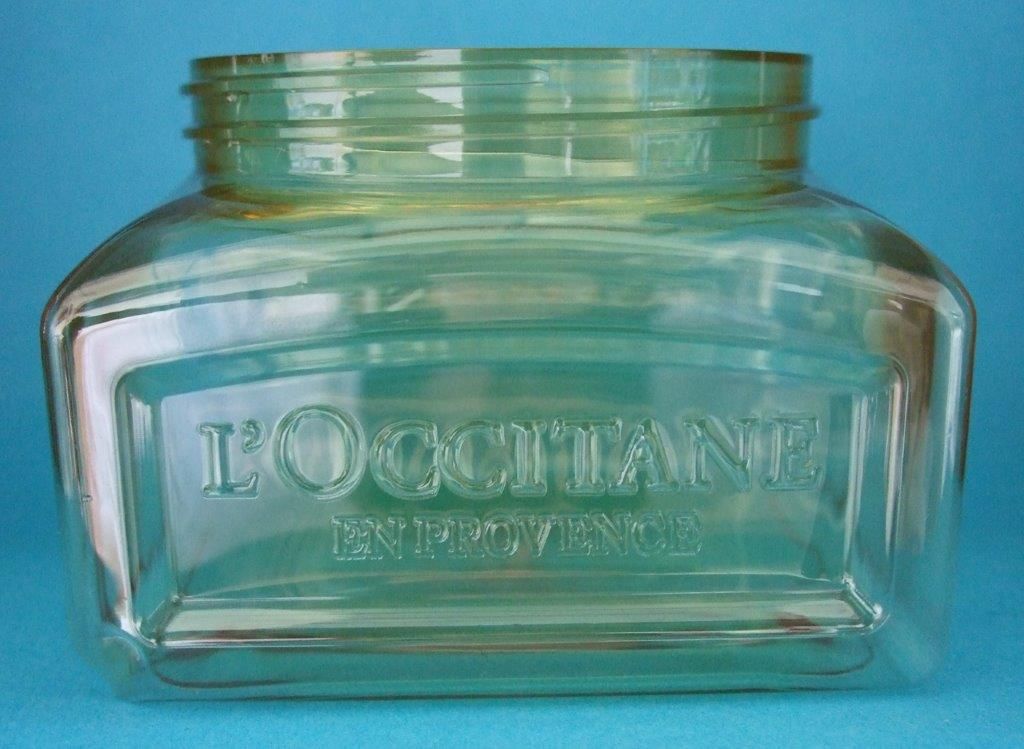 Bouteille rectangulaire en verre transparent avec logo « LOCCITANE » en relief sur fond bleu