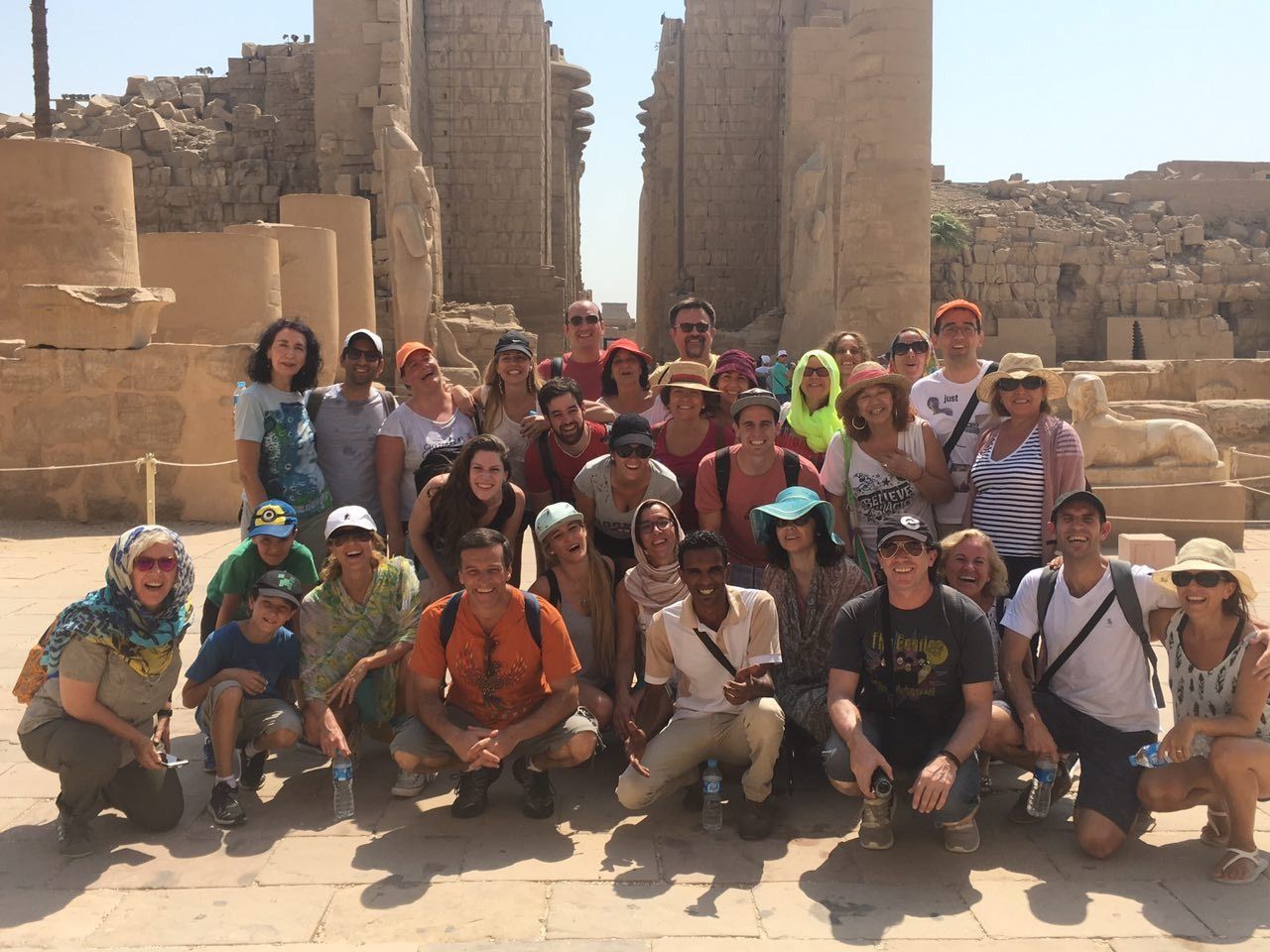 Grupo de personas posando en un templo antiguo. Columnas y estructuras de piedra al fondo. Día soleado.
