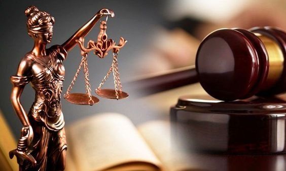 Estatua de la Dama de la Justicia sosteniendo una balanza, un mazo sobre un bloque de madera y un libro abierto parcialmente visible.