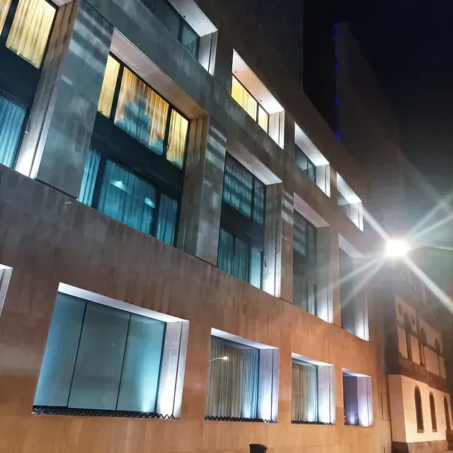 Edificio moderno de noche con ventanas iluminadas, fachada beige y luz de calle brillante.