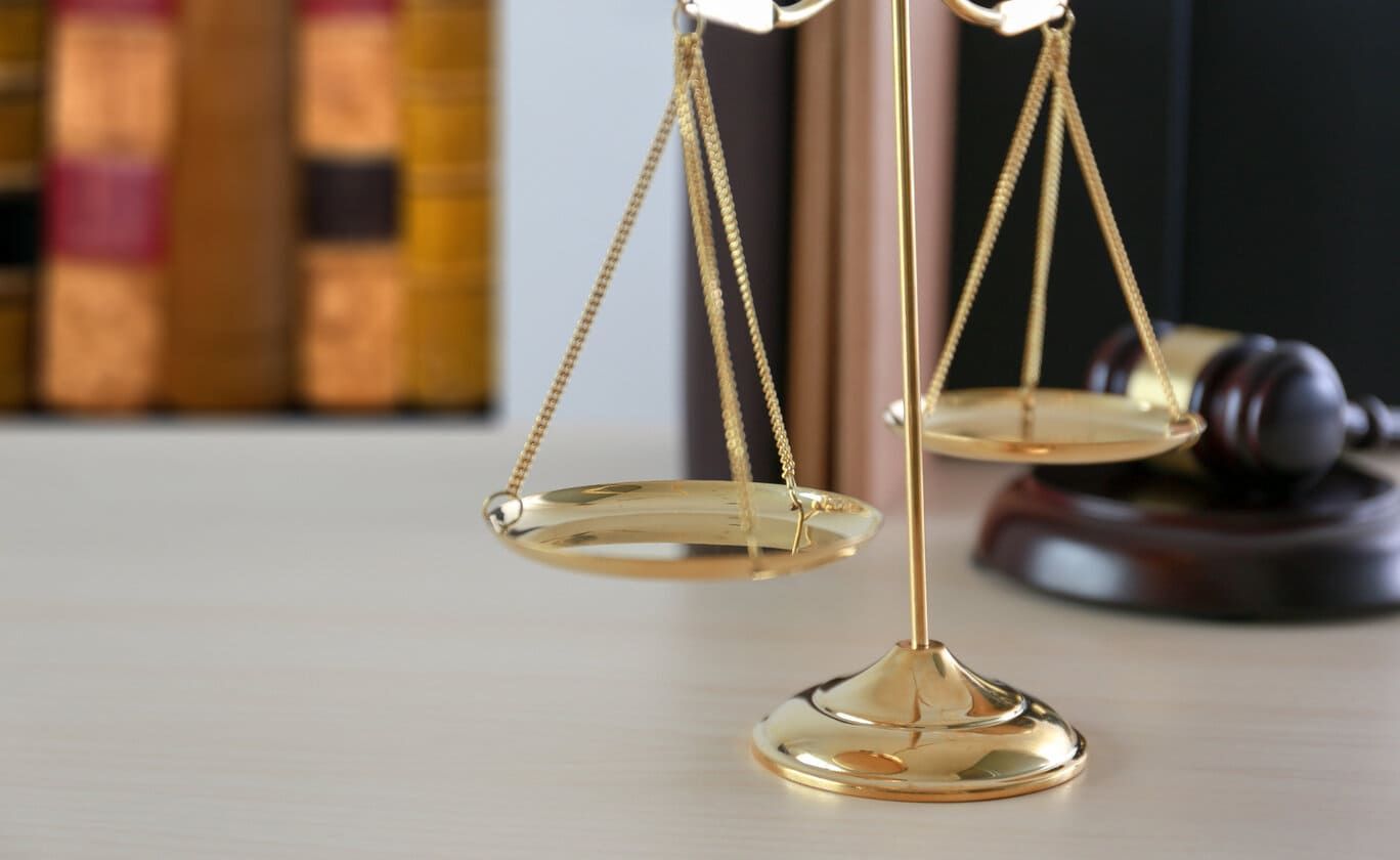 Balanza de la justicia dorada con libros y un mazo en el fondo.