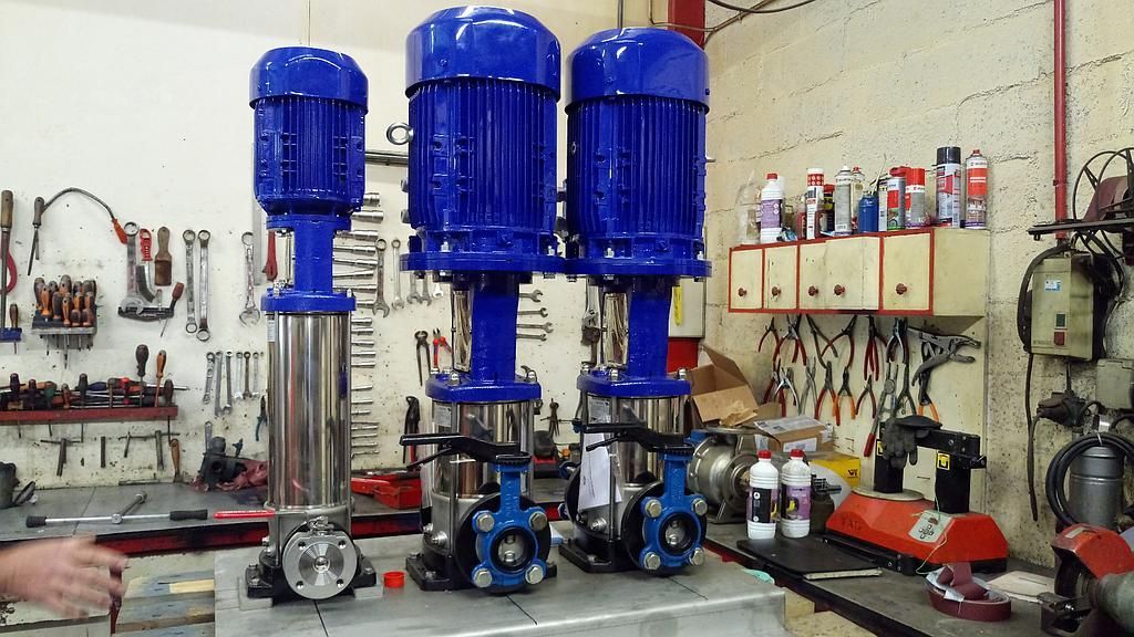 Trois pompes à eau bleues et argentées sur une surface métallique dans un atelier.