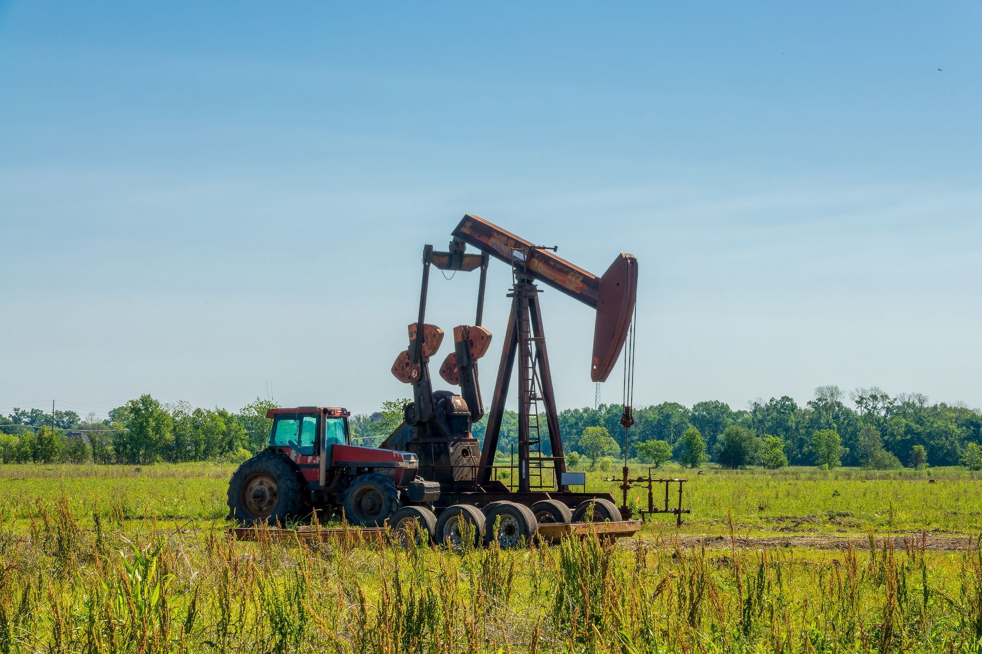 Un chevalet de pompage et un tracteur dans un champ.