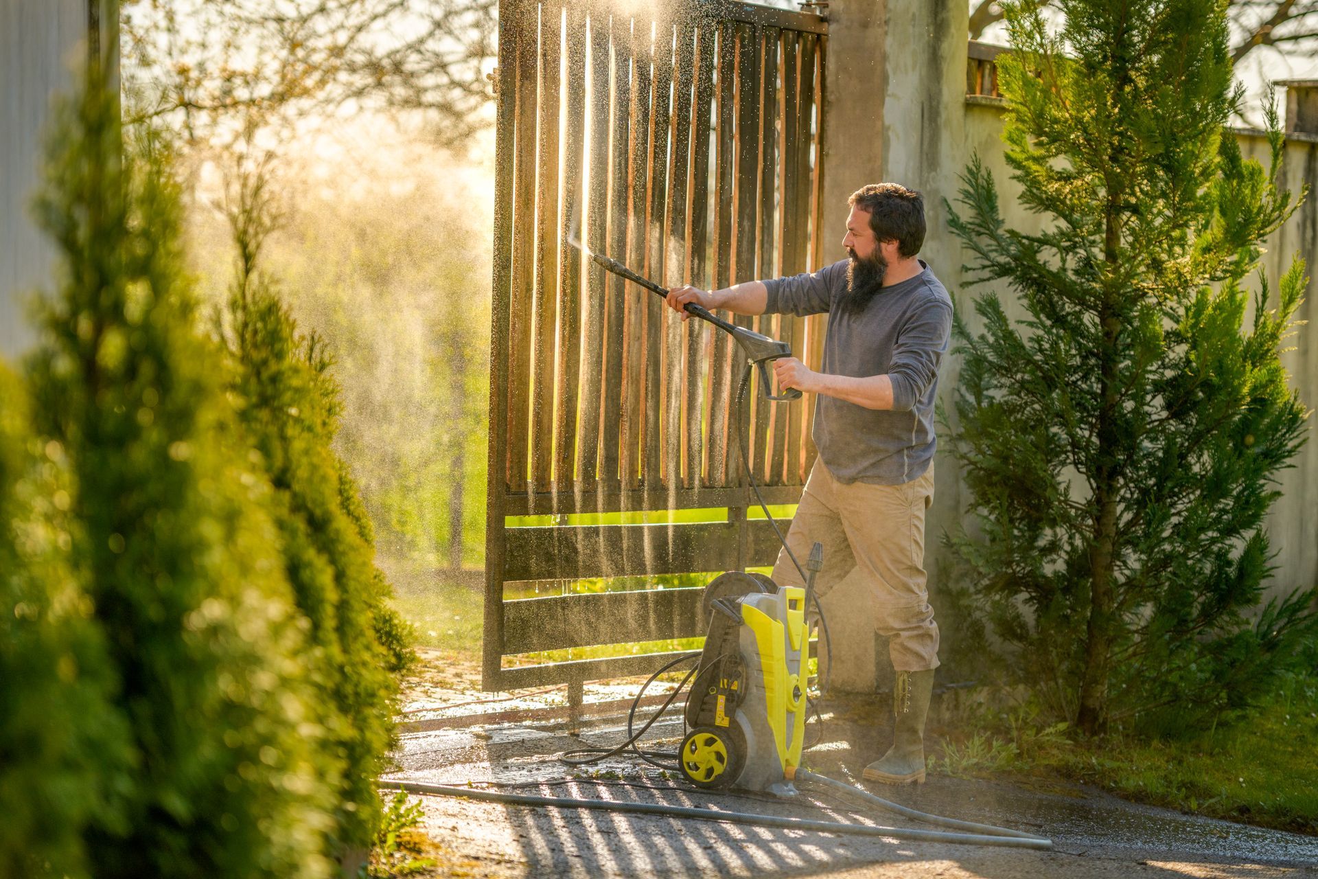 Un homme nettoie un portail en bois avec un nettoyeur à haute pression.