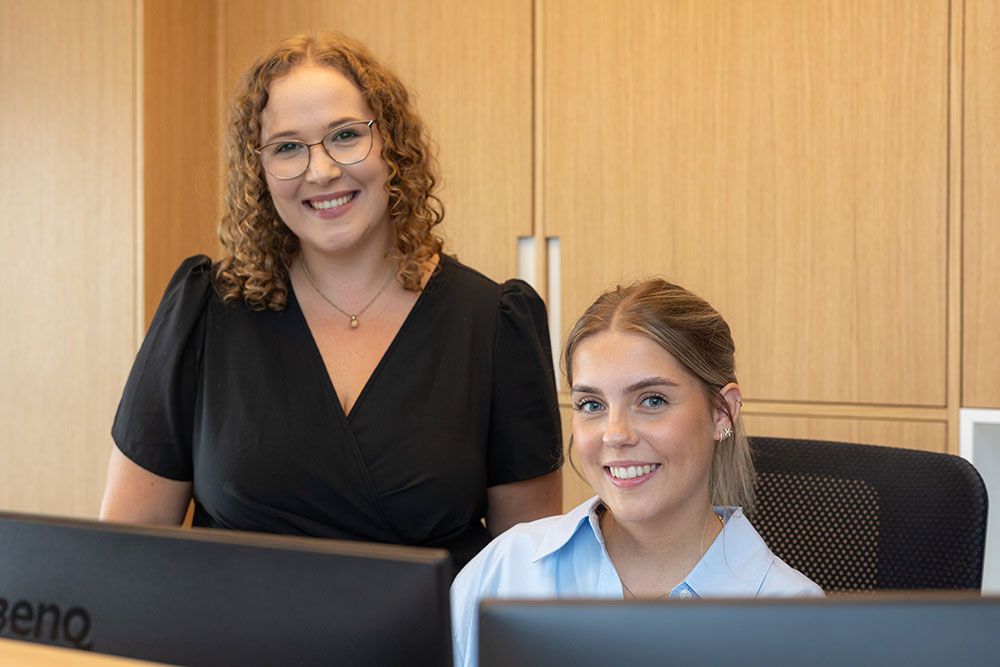 Zwei Frauen stehen nebeneinander vor Computerbildschirmen.