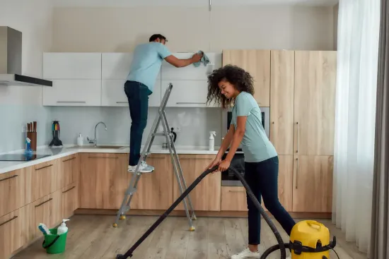 Persona limpiando una cocina: una persona subida a una escalera limpiando los armarios