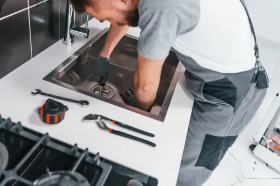 Fontanero trabajando debajo del fregadero de la cocina, utilizando herramientas.