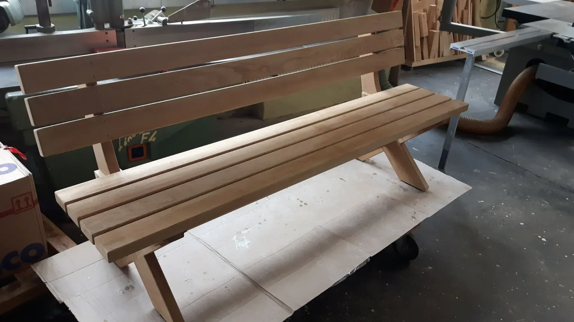 Eine Holzbank mit Rückenlehne, die auf Karton in einer Werkstatt steht.