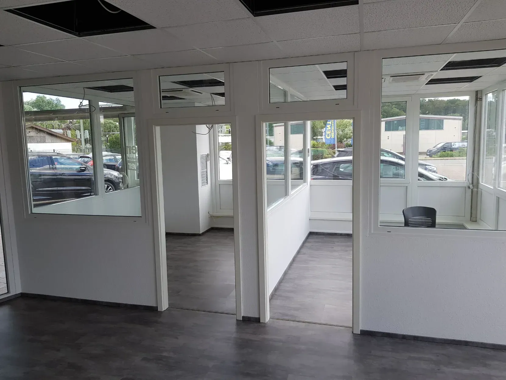 Innenansicht eines Geschäftsraums mit mehreren weiß getünchten Räumen, großen Fenstern und dunklem Bodenbelag.