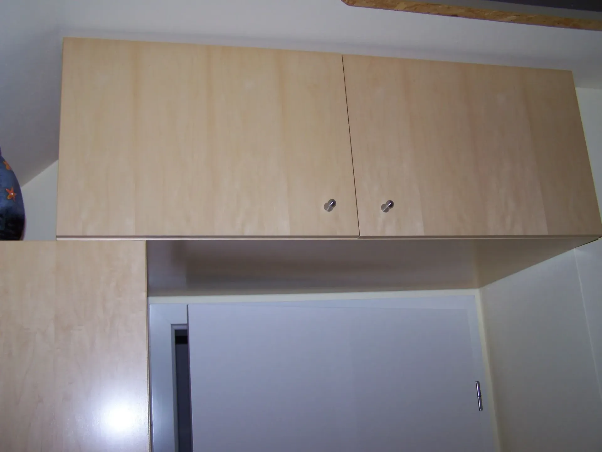 Helle Holzküchenschränke an der Wand. Schranktüren mit silbernen Knöpfen.