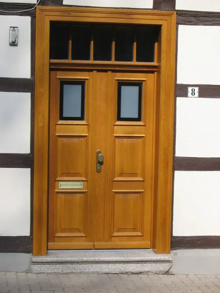 Doppelte Holztür mit Fenstern in einem braunen Rahmen an einem Fachwerkhaus mit Steintreppe.